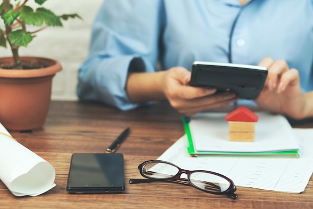 A person using a calculator and reviewing financial documents on a desk, with a homeownership contract visible in the background.