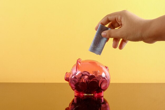 A close-up shot of a hand inserting coins into a piggy bank. The background is blurred and shows a calendar with the month of January highlighted, symbolizing the anticipation of the new year and increased savings opportunities.